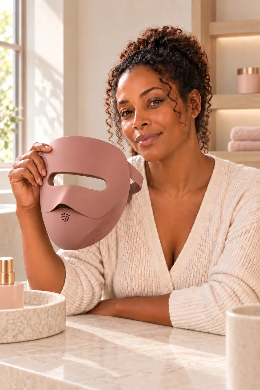 Woman holding the rose-brown LED mask at her vanity